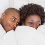 african american couple laying in bed under covers