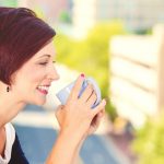 brunette woman drinking coffee outside on balcony