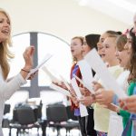 middle aged woman teaching a choir of students