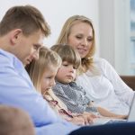 mother and father sitting on sofa with two children