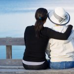 mother and grown daughter sitting on pier