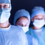 three surgeons in blue gowns and masks