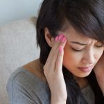 woman sitting on sofa suffering from migraine headache