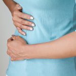woman wearing blue top having stomach pains
