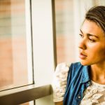 young woman looking out window while thinking