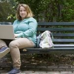 young woman sitting on a bench in a park with a laptop